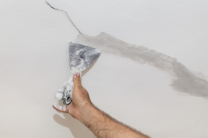 Particulier rebouchant les fissures dans son mur
